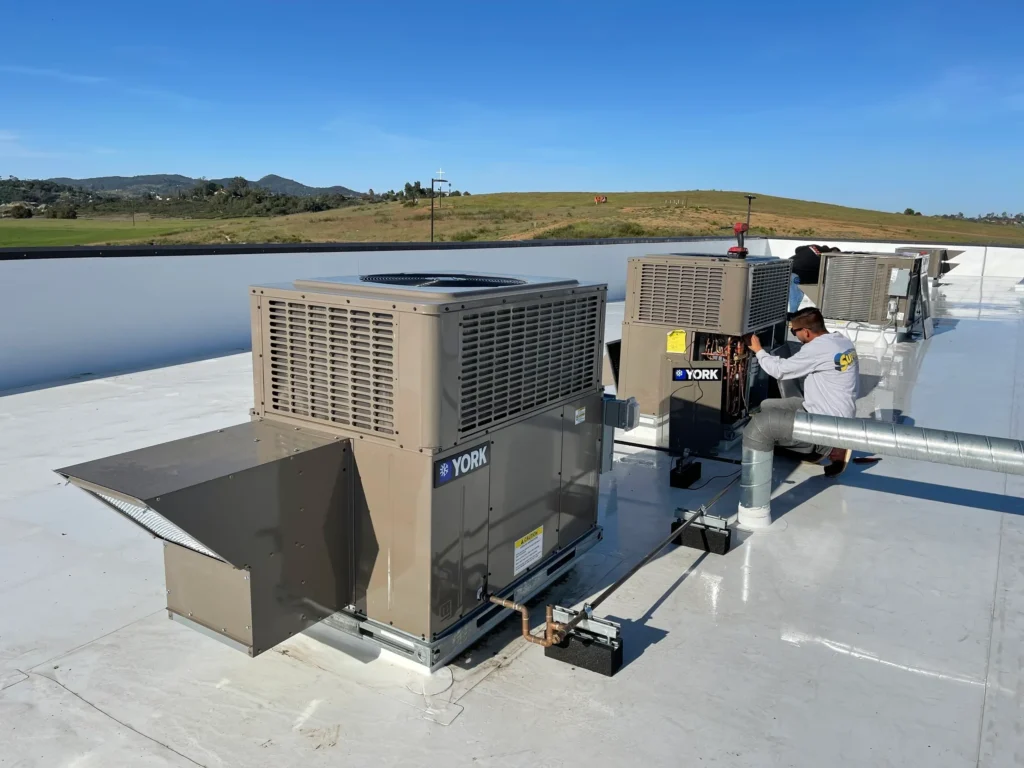 A technician works on commercial packaged rooftop air conditioning units on a flat roof.